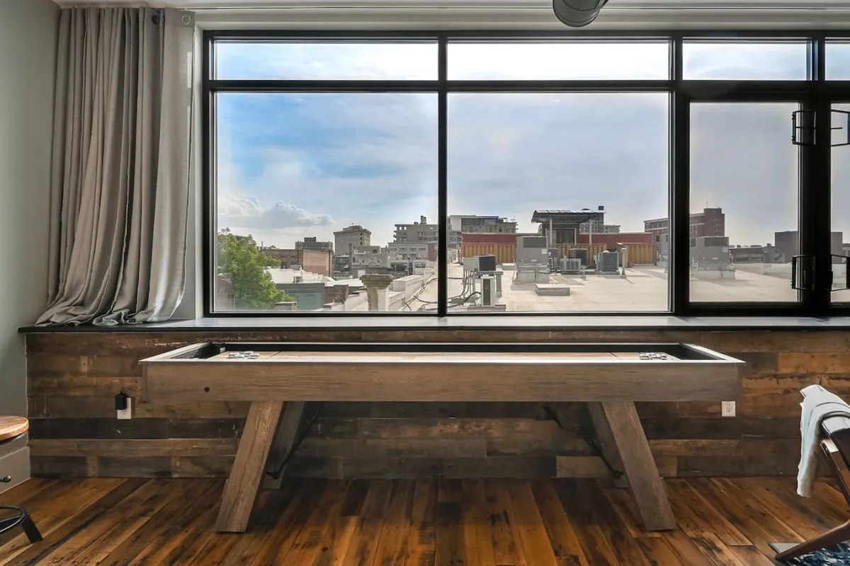 This image features a large window that offers city views, with a shuffleboard table in the foreground. The mood is playful and relaxed, inviting guests to unwind and connect while enjoying the vibrant atmosphere of downtown just outside.