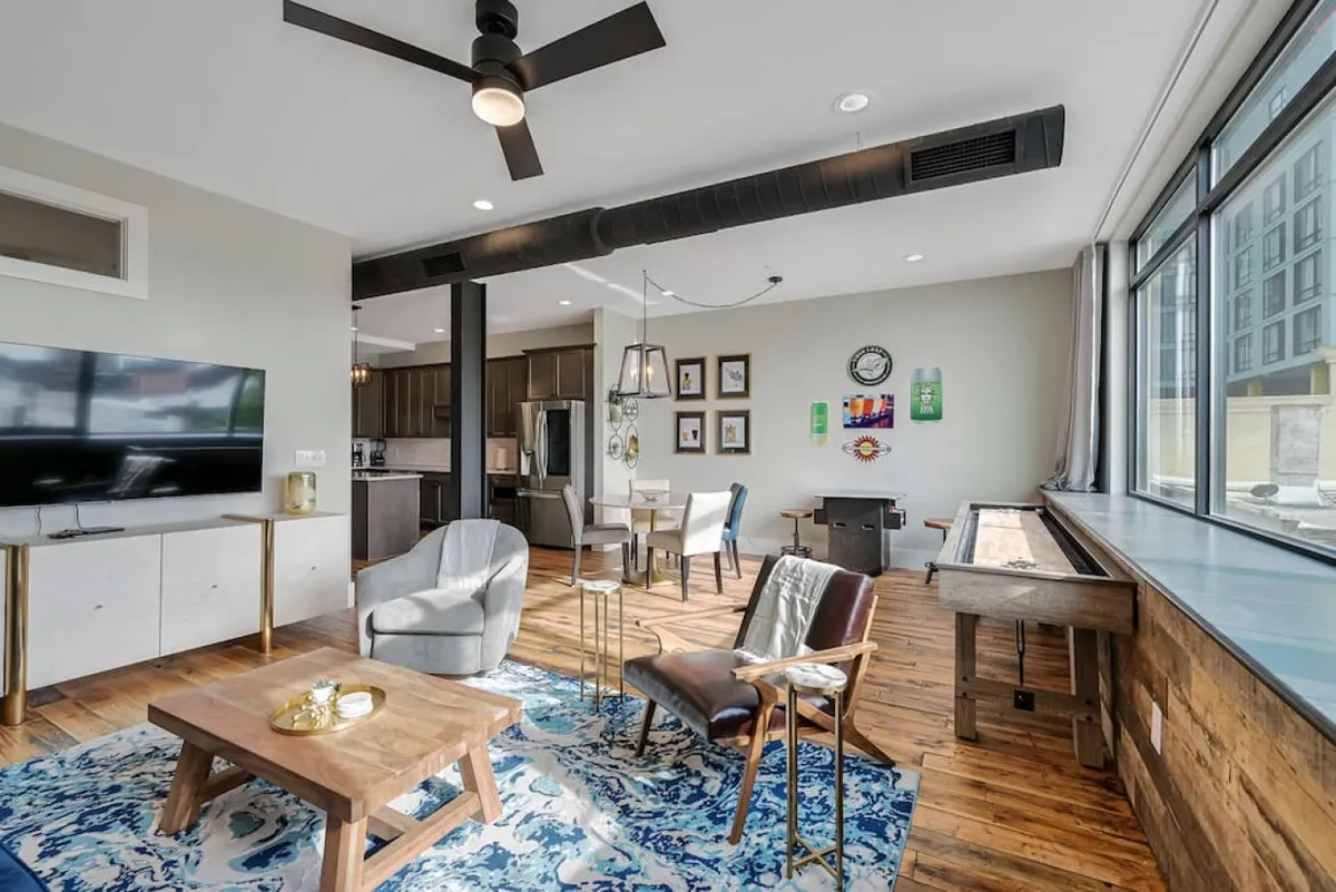 A large window fills the combined living and dining area with natural light, while a TV unit, distinctive area rug, and inviting dining setup create a space ideal for both socializing and relaxing. The view showcases both areas together, emphasizing openness and togetherness.