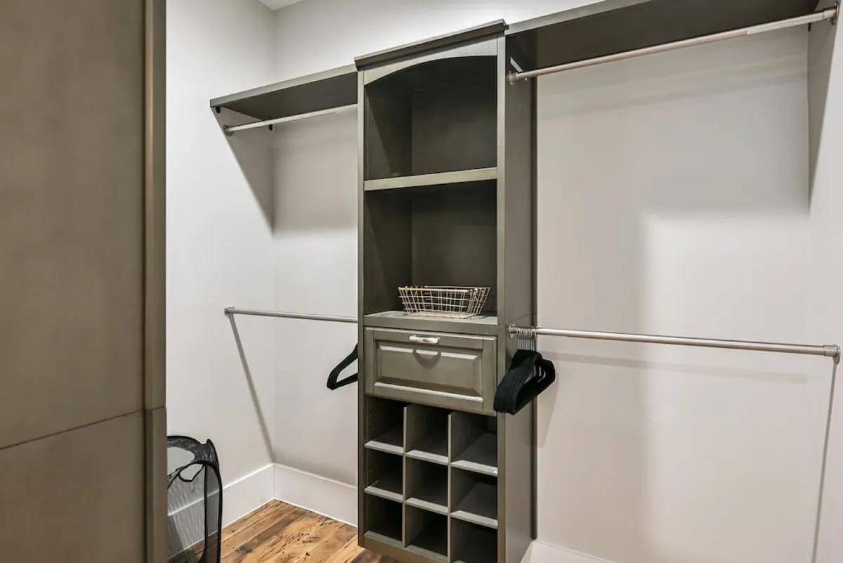 This image showcases a spacious, organized storage unit with hanging rods and wooden flooring. The environment is clutter-free, designed for ease of storing and accessing personal items, and could be adjacent to an entryway or garage area.