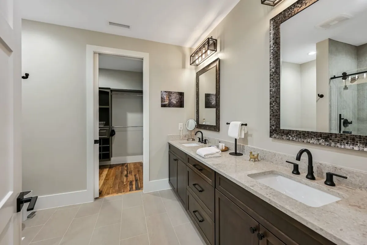 A spa-inspired bathroom with a double vanity, expansive mirrors, decorative lighting, and a glimpse of a walk-in closet. The space feels serene and elegant, designed for indulgent self-care routines and an elevated daily experience.