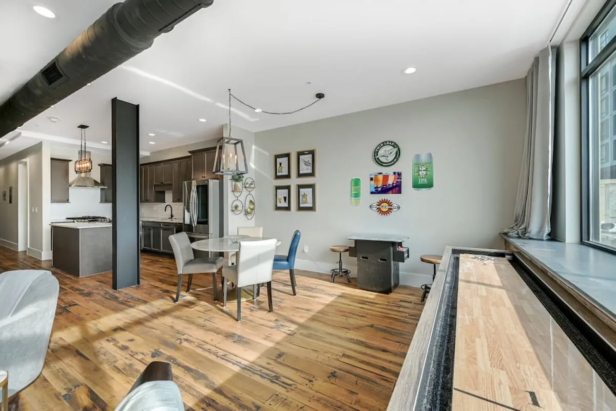 A contemporary dining area with a table set near sliding windows, art-adorned walls, and an open kitchen. The bright natural light hints at the city just beyond, and the space is styled for social gatherings, meals, or leisurely moments at home after a day out.